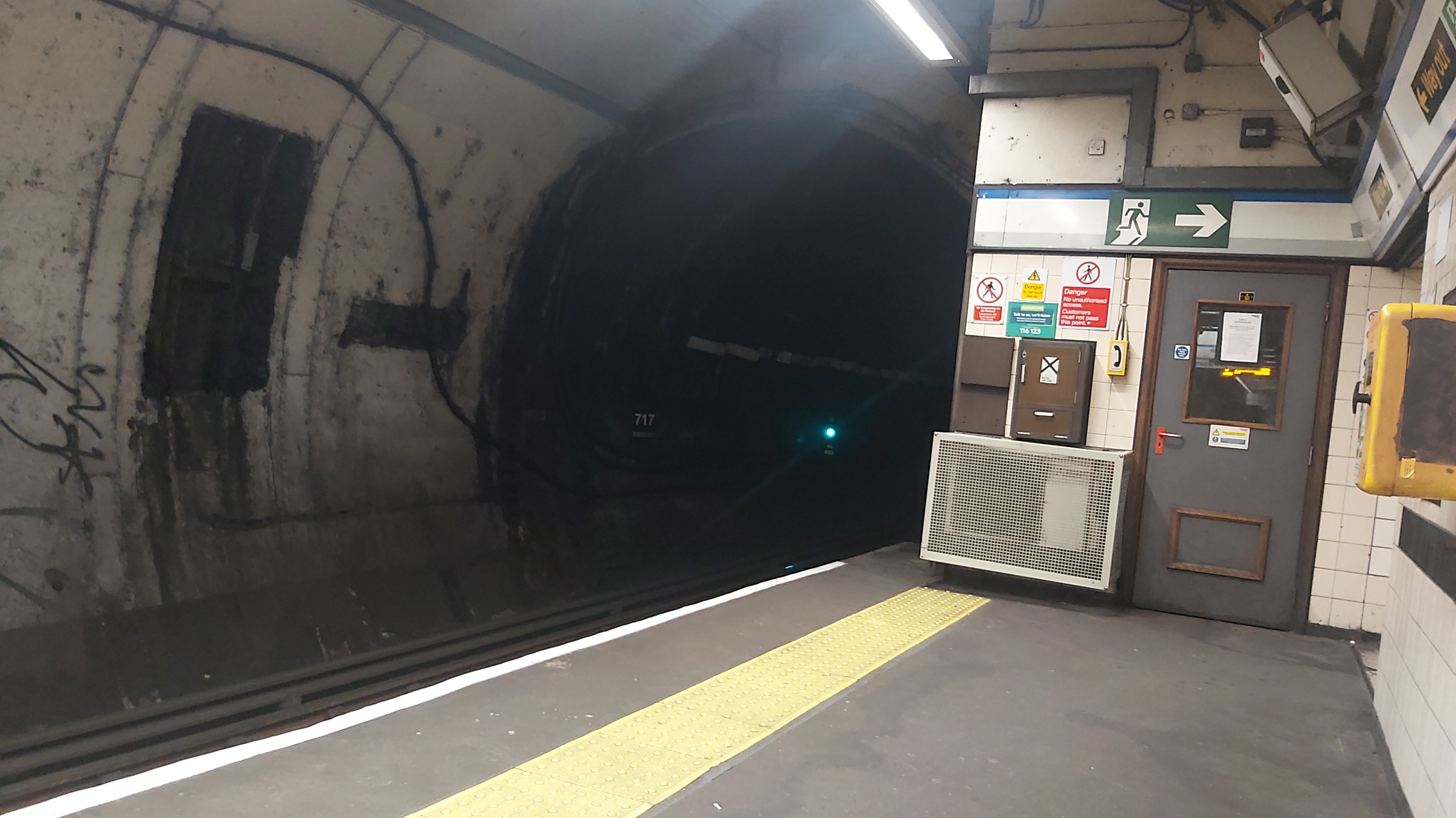 The entrance to the tunnels heading south at Highbury & Islington. A door, some signage, and an emergency exit sign is also visible.